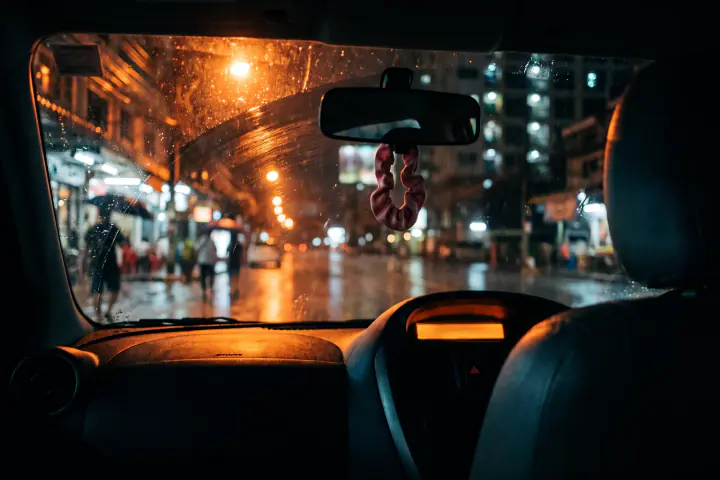 ในรถยามค่ำที่ฝนตก แสงไฟถนนสีส้มไหลผ่านกระจกหน้า ไฟหน้าปัดเรืองนวลโดยไม่เห็นตัวเลข เบาะข้างคนขับว่าง มียางรัดผมสีชมพูซีดคล้องอยู่ที่กระจกมองหลัง